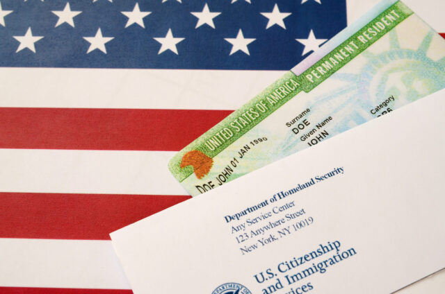 United States Permanent resident green card from dv-lottery lies on United States flag with envelope from Department of Homeland Security close up