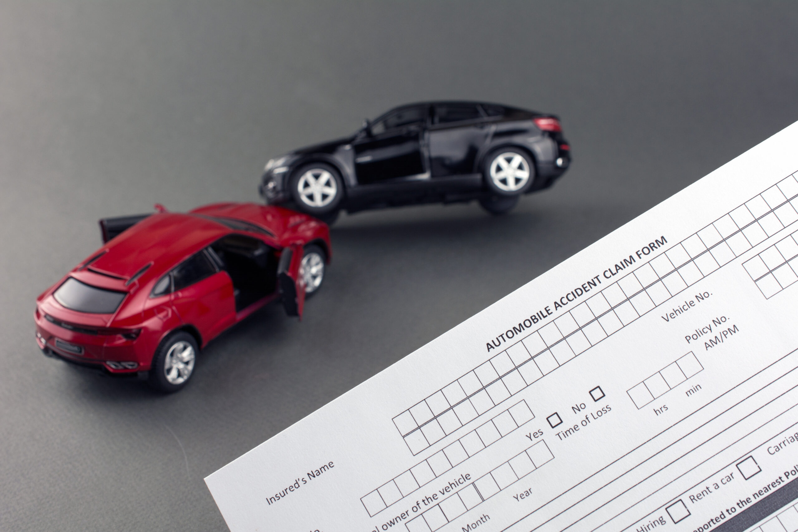 two toy broken cars and car insurance document. compare car insurance concept. gray background.