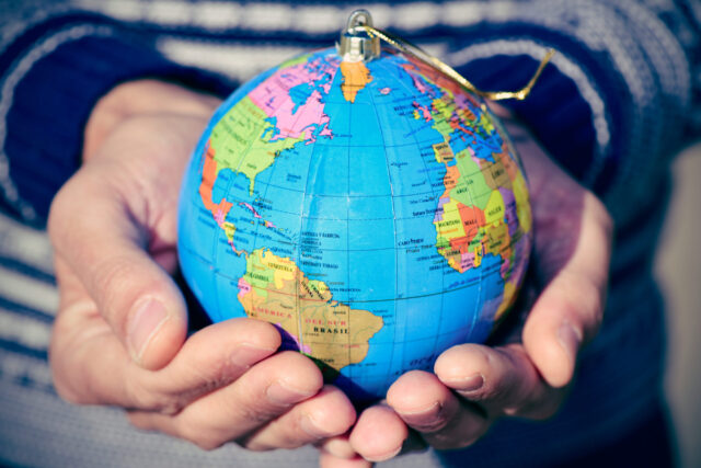 closeup of a young caucasian man with a world globe with a golden string as a christmas ball in his hands
