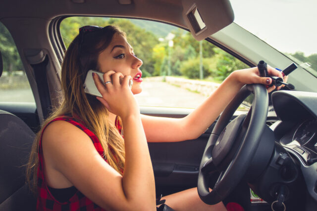 Profile view of a reckless Caucasian young woman using a smartphone while driving a car