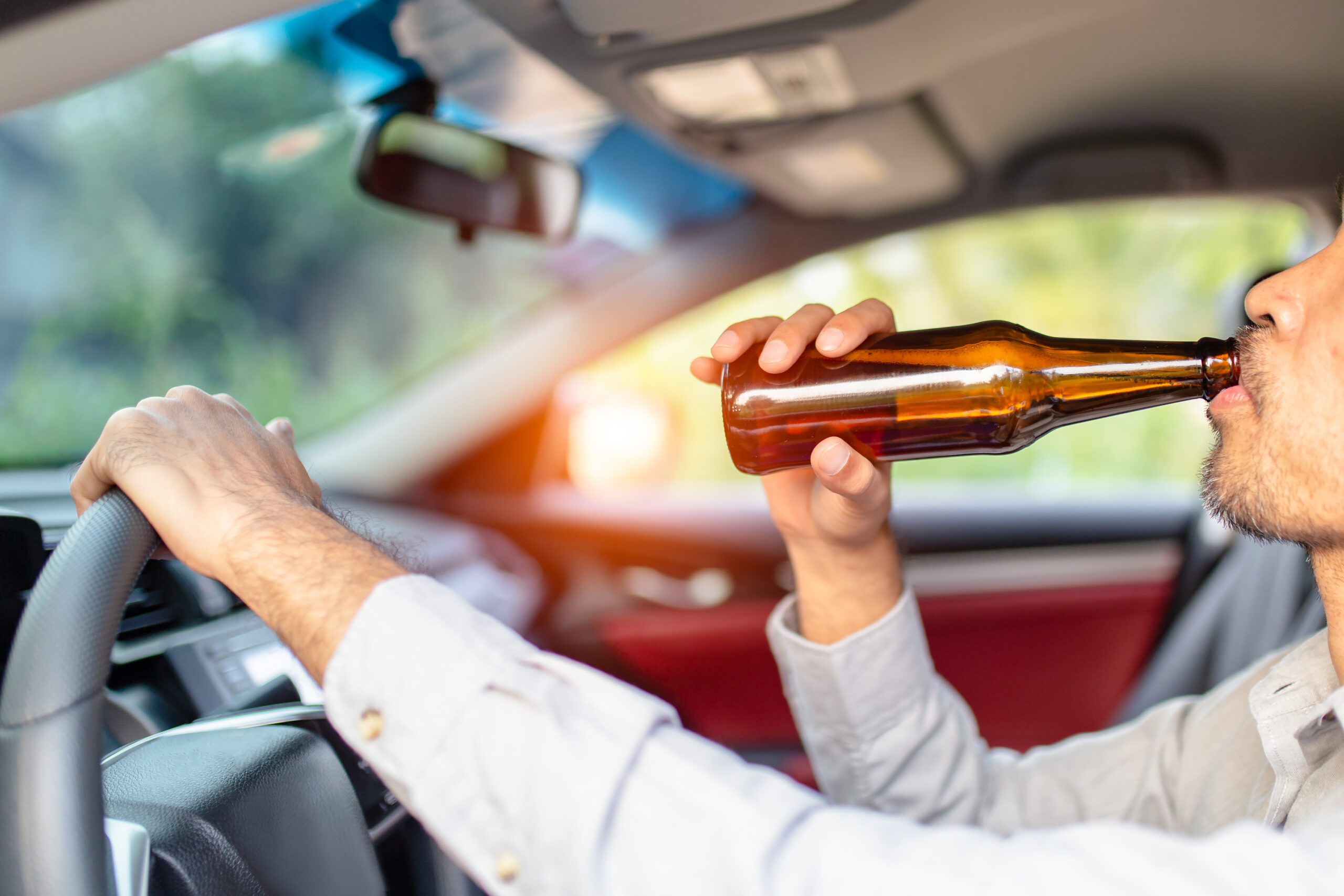 Drunk young man drives a car with a bottle of beer with sunset background, Dangerous driving concept
