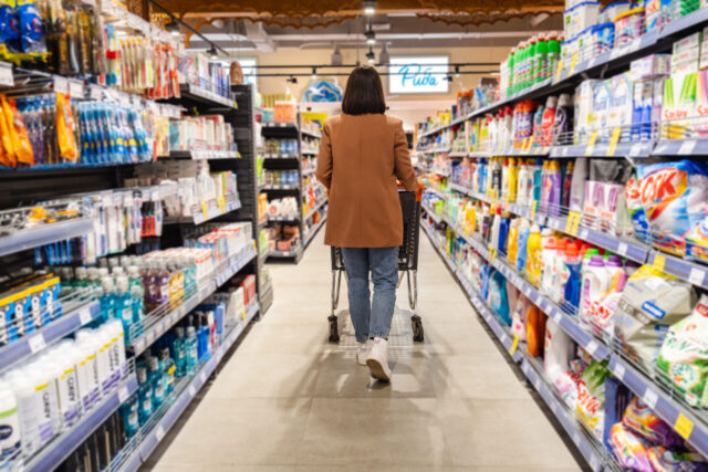 a woman with a cart back view walks between rows of shelves in a grocery store
