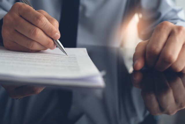Closeup image of Businessman signing official rental contract. Corporate man writing on buiness document with a pen and working in modern office with reflection on desk. front view
