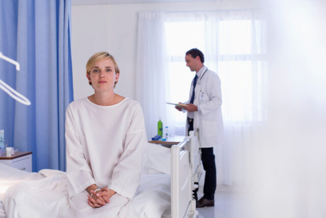 Portrait serious young female patient sitting on edge of hospital bed